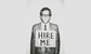 A man in a suit and glasses wearing a sign that says "hire me" 